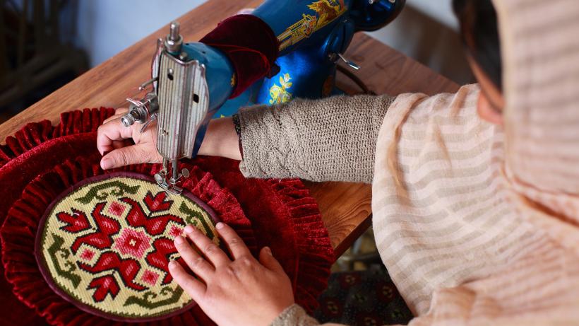 A woman sewing a pillow cover with a machine in Pakistan.