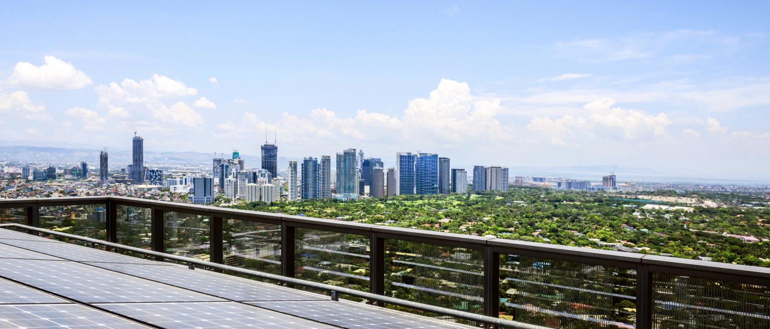 Solar panels and Manila cityscape under blue sky, Philippines. Photo credit: Mint Images / Mint Images RF via Getty Images.