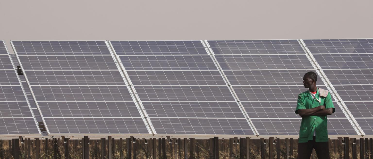 People stand next to solar panels of the solar energy power plant in Zaktubi, near Ouagadougou
