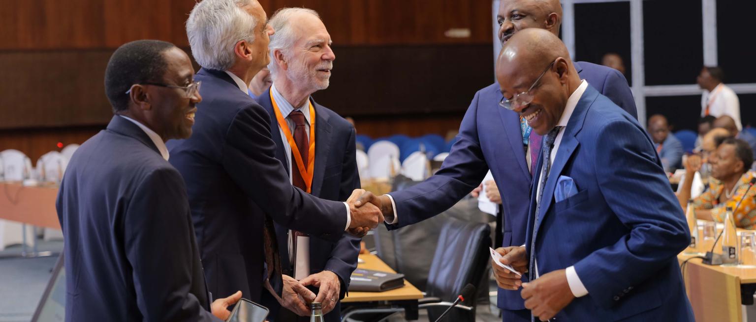 An image of 5 men shaking hands at an economic development conference held by the IGC in Uganda. 