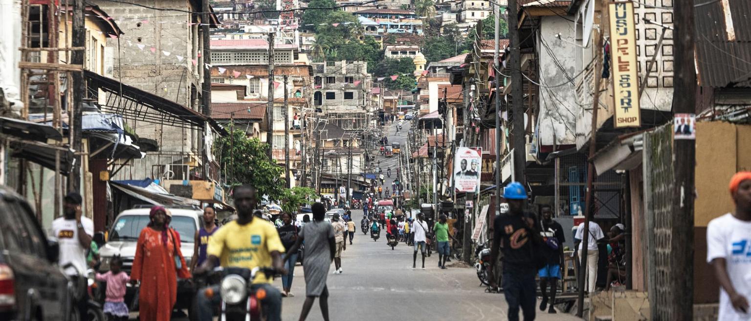 People walking down a busy street with businesses reliant on electricity in Freetown, Sierra Leone.