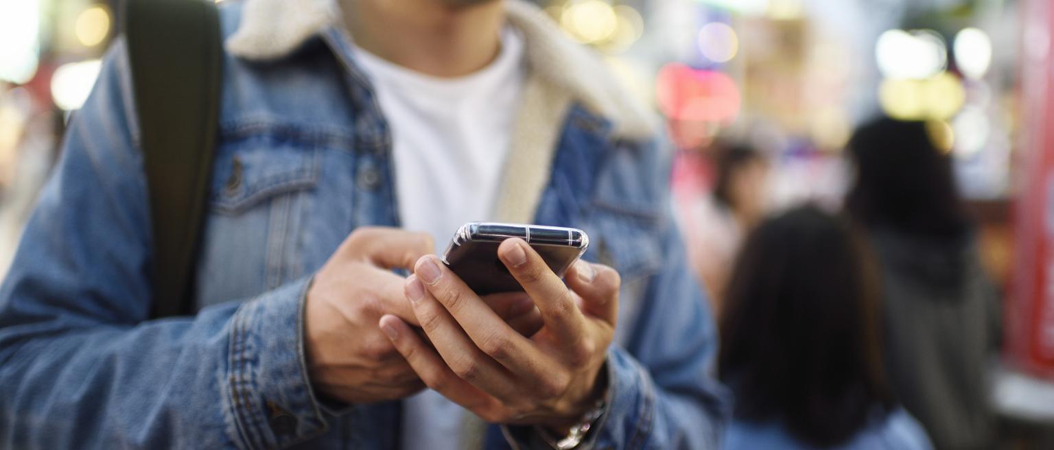 Man using his mobile phone in busy shopping district at night - stock photo