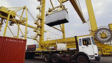 A container being lifted from a shipping lorry surrounded by cranes and other shipping cargo.