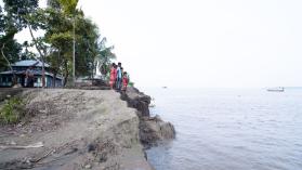 People standing at the edge of a river bank that has eroded due to climate change, in Bangladesh