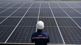 An engineer in a white helmet and blue uniform is looking out over a photovoltaic panels