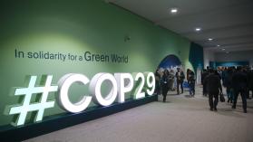 People attending the COP29 UN Climate Change Conference, walking past the event tagline written on the wall 'In solidarity for a Green World'g past the 