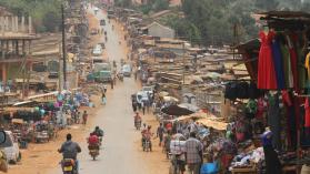 People on motorcycles on a road next to market stalls