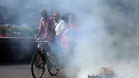 Increasing air purifier adoption could help severe air pollution illustrated by rubbish burning beside the main road in the Dhaka University area in Dhaka, Bangladesh as a rickshaw cycles past with passengers wearing face masks.