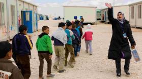Syrian children looking away walking in single file as they exit a class at a Jordan refugee camp, Zaatari, as a teacher waves them on.