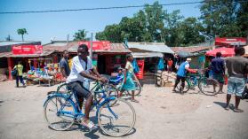 How rural migrants are integrating in Quelimane, Mozambique as a man on a stationary bicycle looks on at a colourful market with traders in the background.