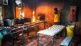 Electrification in rural South Africa is slow, demonstrated by a man overlooking a kitchen using fire to cook. 