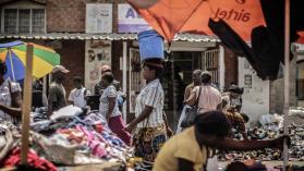 An image of a woman carrying a bucket on her head as she walks through a market in Zambia. 