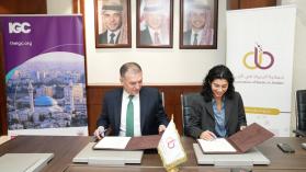 Two people sat a desk signing an MoU between ABJ and IGC flanked by branded banners.