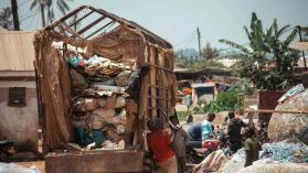 Group of people in a garbage sorting plant next to bags of plastic bottles and a truck with waste paper.