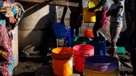 A group of people in Zambia waiting to collect water in buckets in an urban area during a cholera outbreak demonstrating the risk to health during flooding.