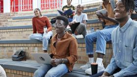 Smiling young multi-ethnic students enjoying while sitting on amphitheater at university campus. Photo credit: Klaus Vedfelt / DigitalVision via Getty Images.