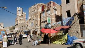 People walking past a decorated house and market stall in Sanaa, Yemen.