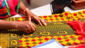 A tailor's hands marking colourful ankara fabric with chalk on a workspace in Ghana
