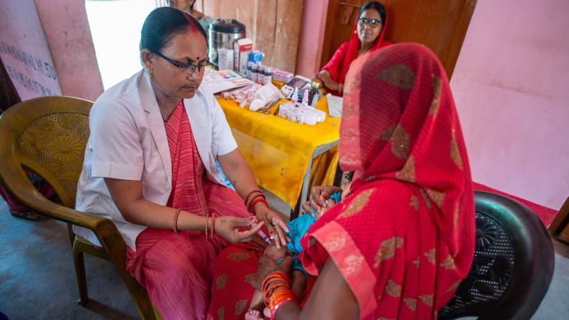 Mother holds child while health worker administers an immunisation shot