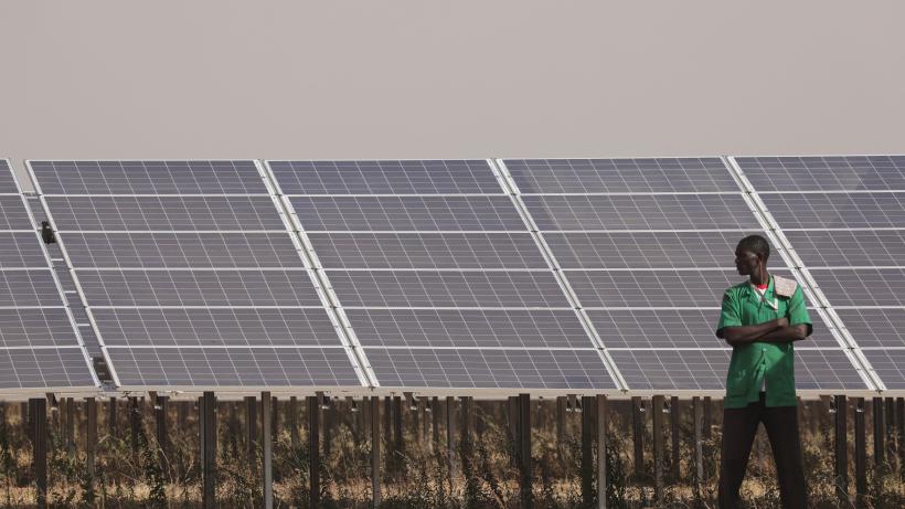 People stand next to solar panels of the solar energy power plant in Zaktubi, near Ouagadougou