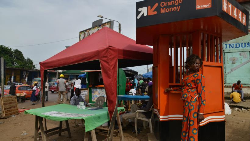A woman dressed in orange withdraws money at an Orange Money cashier booth
