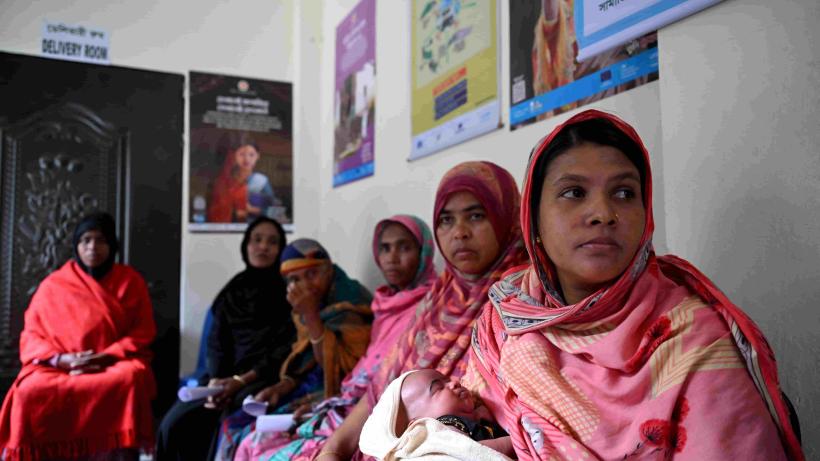 The impact on paid maternity leave on women in Bangladesh could be significant for this woman who waits in a clinic with other women, holding a newborn baby.