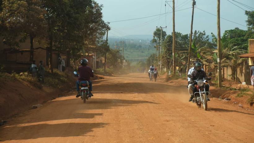  How distance affects public service delivery illustrated by locals driving motorbikes on a dusty road in Bunjako, Mpigi district, Uganda. 