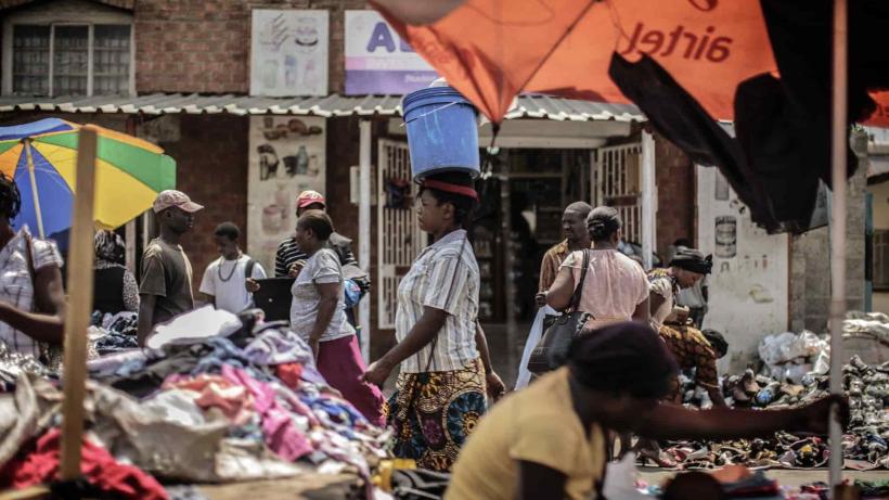 An image of a woman carrying a bucket on her head as she walks through a market in Zambia. 