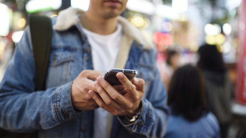Man using his mobile phone in busy shopping district at night - stock photo