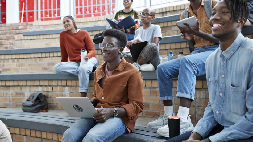 Smiling young multi-ethnic students enjoying while sitting on amphitheater at university campus. Photo credit: Klaus Vedfelt / DigitalVision via Getty Images.