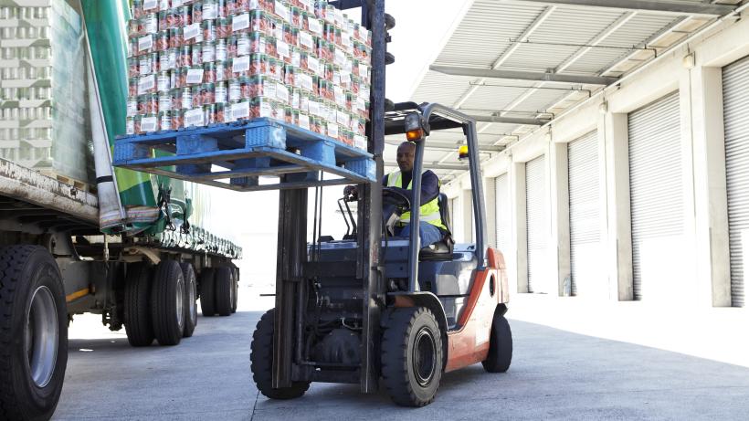 Fork lift truck loading a pallet of tinned tomatoes onto a lorry outside a large food distribution warehouse. Photo credit: Alistair Berg / DigitalVision.