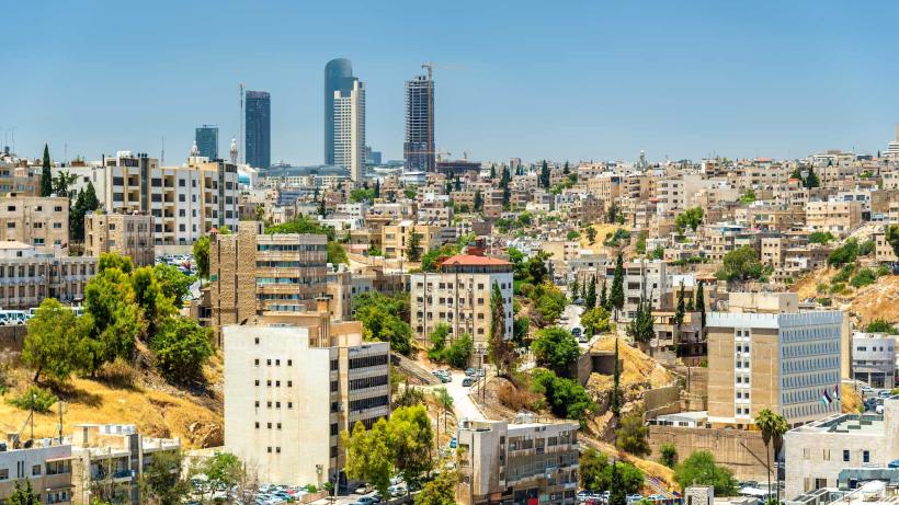 A view of Amman's skyline with many buildings and a few tall skyscrapers under a clear blue sky.