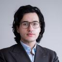 A profile photo of a man with dark hair wearing glasses in a dark suit.
