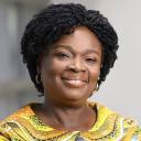 IGC Zambia Country Director Victoria Kwakwa in yellow smiling at camera.