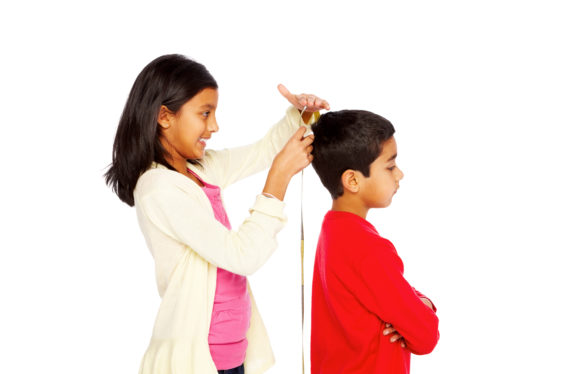 Cute little girl measuring height of her young brother on white background