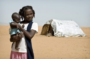 A young girl in Sudan holding a baby near a USAID tent in the Al Salam IDP (Internally Displace Persons) camp. Photo credit: Sven Torfinn